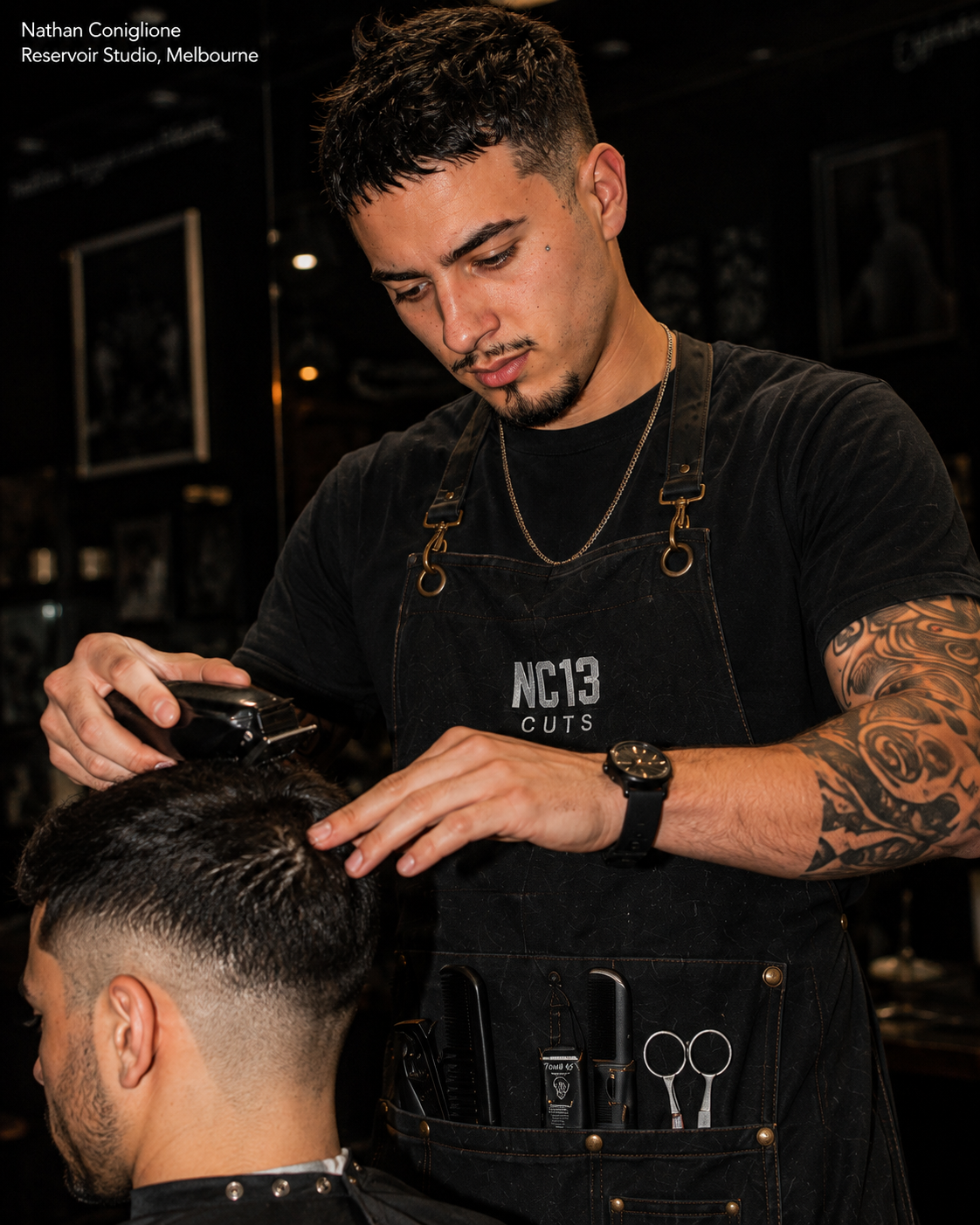 Nathan Coniglione clipper-cutting a client's hair in his Reservoir studio, wearing a black NC13 CUTS apron.