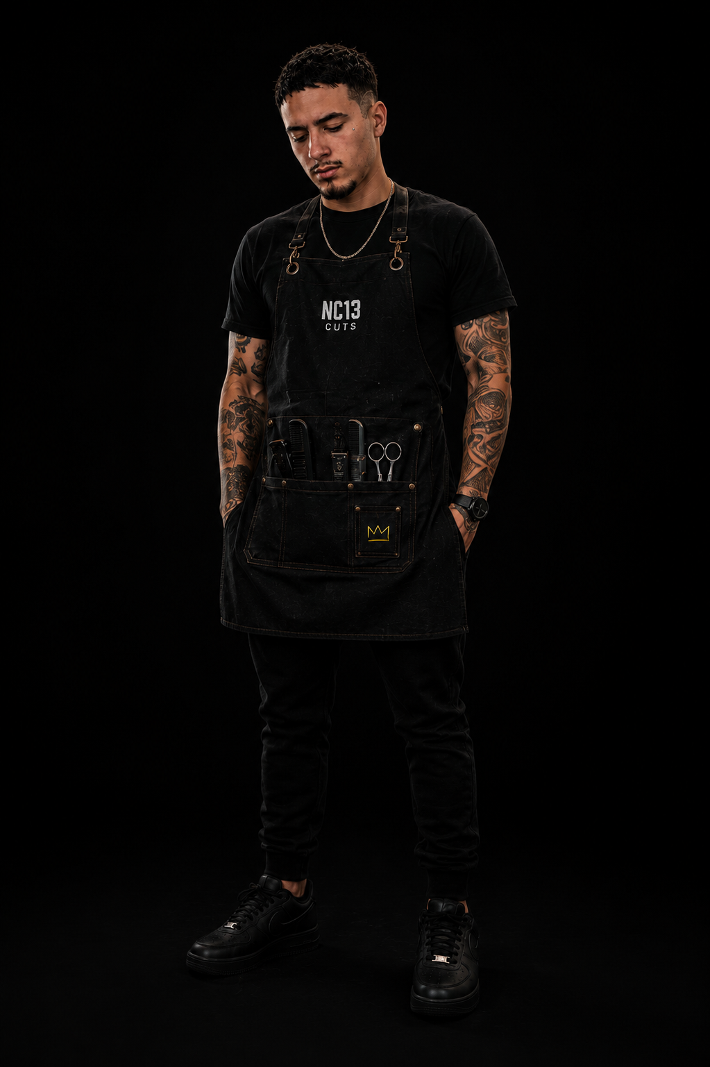 Full-length portrait of Nathan Coniglione in black, wearing his NC13 CUTS apron with tools in the pockets.